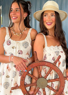 Two women in matching dresses holding a ship's wheel on a dock.